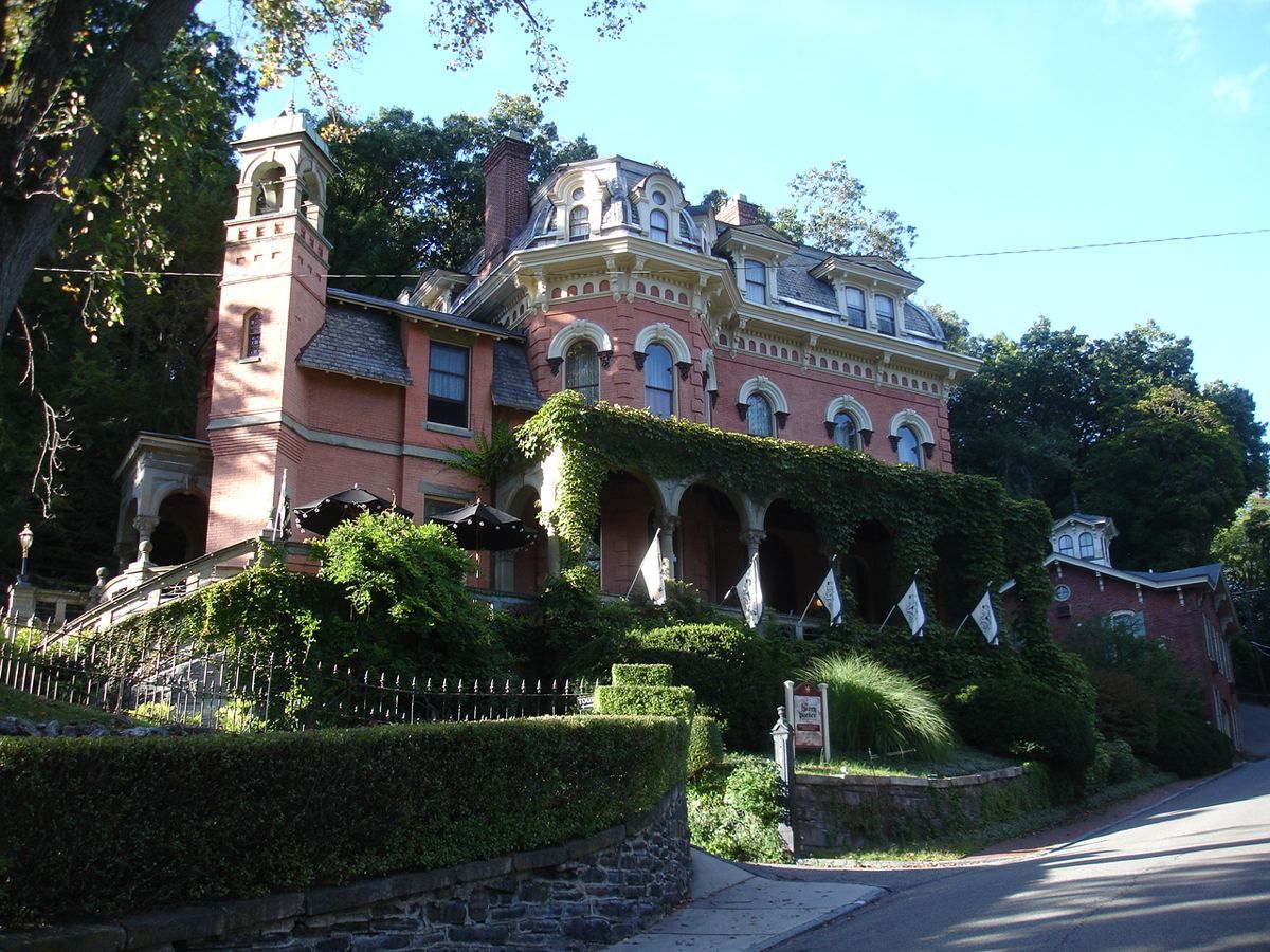 The Harry Packer Mansion, a red-brick Italianate villa with a green-shaded porch and turret, on a wooded slope.