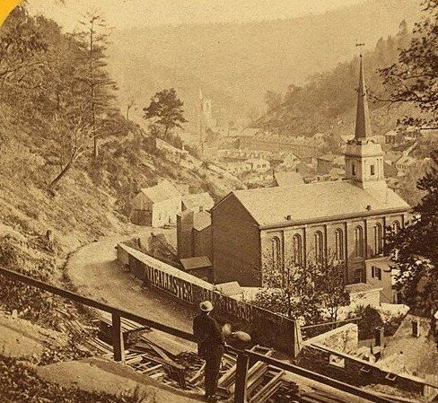 Nineteenth-century view of Mauch Chunk: a church spire, tight rows of houses and railway track running along the valley floor.
