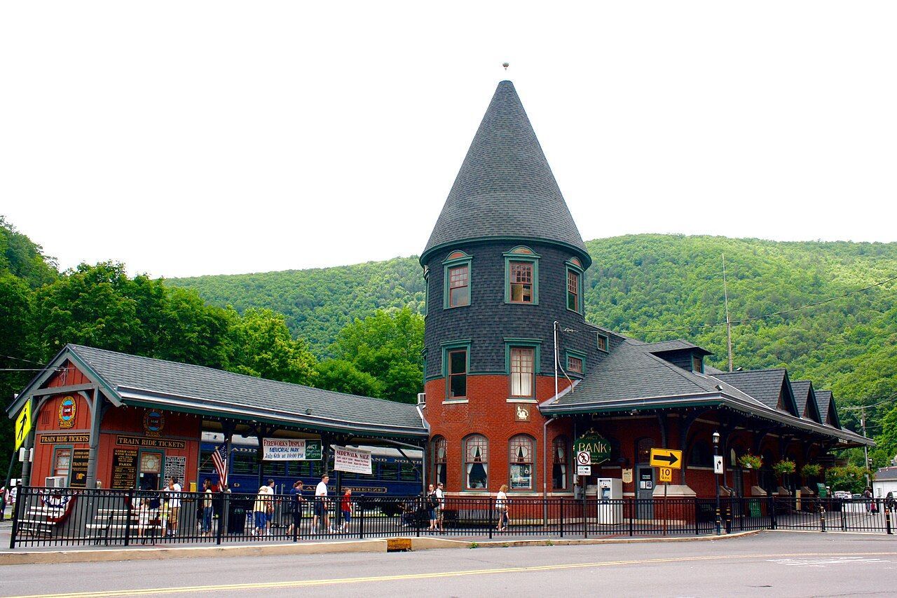 The Central Railroad of New Jersey station in Jim Thorpe — a red brick Victorian depot with a slate turret, the wooded ridge rising behind it.