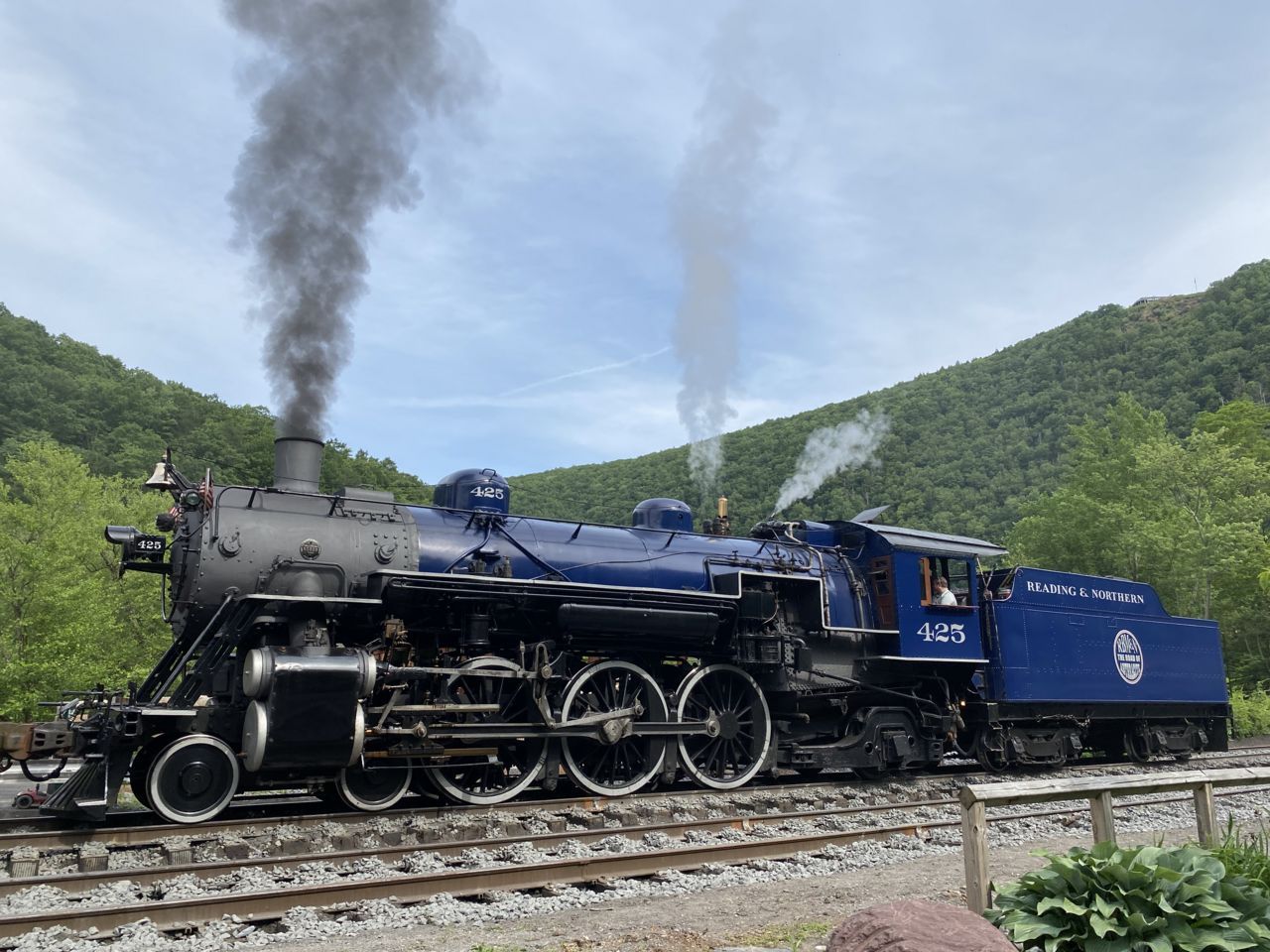 A steam locomotive under full steam on the line beside the river at Jim Thorpe, wooded ridges behind.