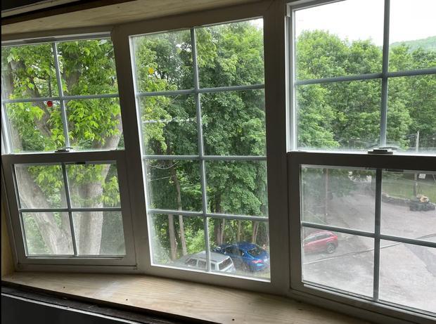 Wide bank of tall multi-pane windows looking out onto trees and the street below.