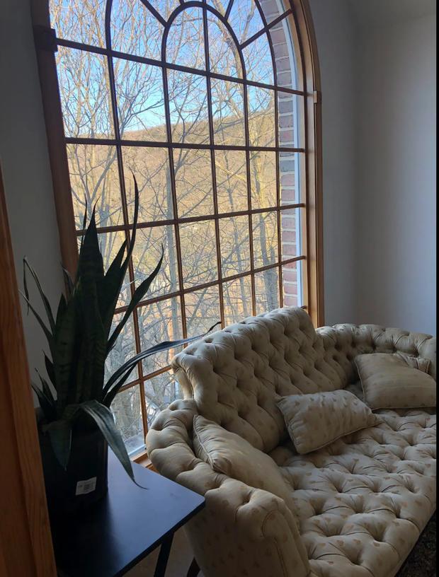Sitting room with a buttoned sofa and a tall arched window looking out to the hillside.