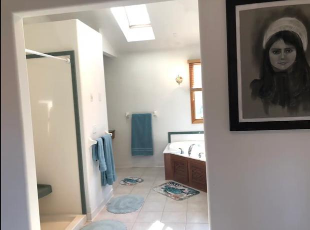 Landing with a large framed portrait on the wall beside a skylit bathroom with a corner tub.