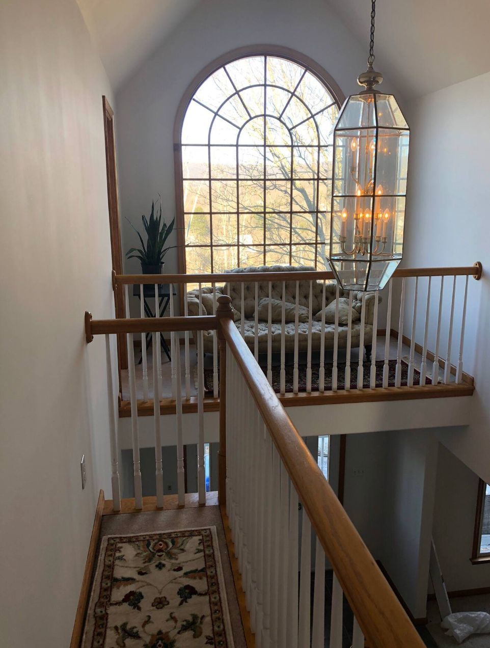 Open staircase and galleried landing beneath a tall arched window with a hanging lantern.