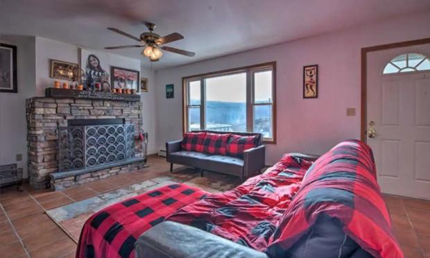 Living room with a stone fireplace, plaid throws and windows facing the hillside.