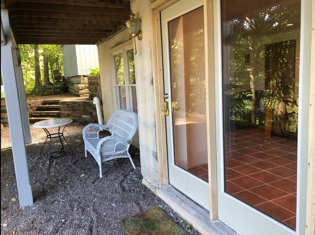 Sliding glass doors opening from the apartment onto a shaded patio with garden chairs.