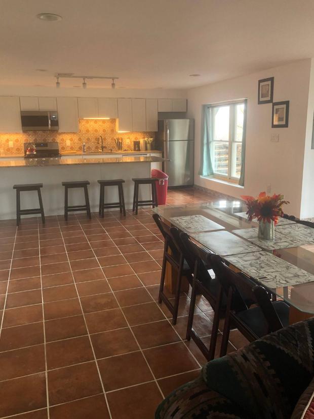 Kitchen with a breakfast bar and stools beside a dining table under a window.