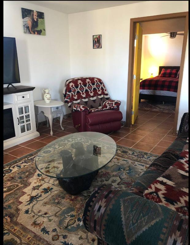 Sitting area with a glass-topped table, sofa and an open doorway into a bedroom.