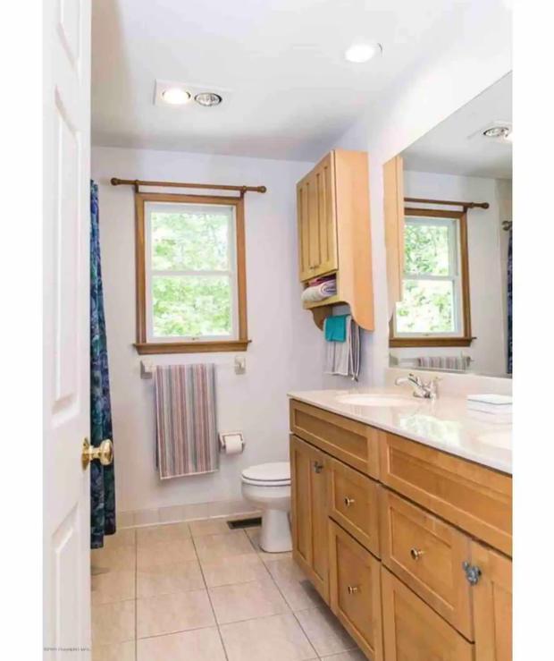 Bathroom with a long vanity, wide mirror and a window over the tub.
