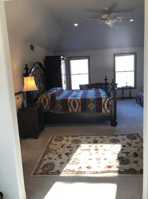 Bedroom with a dark bed frame, patterned rug and sunlight across the floor.