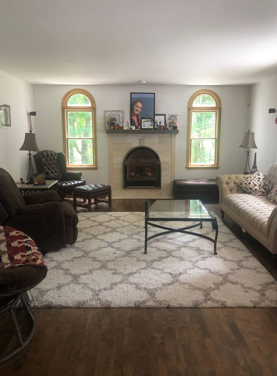 Living room with a stone gas fireplace under a ceramic arch, tall arched windows and pale hardwood floors.